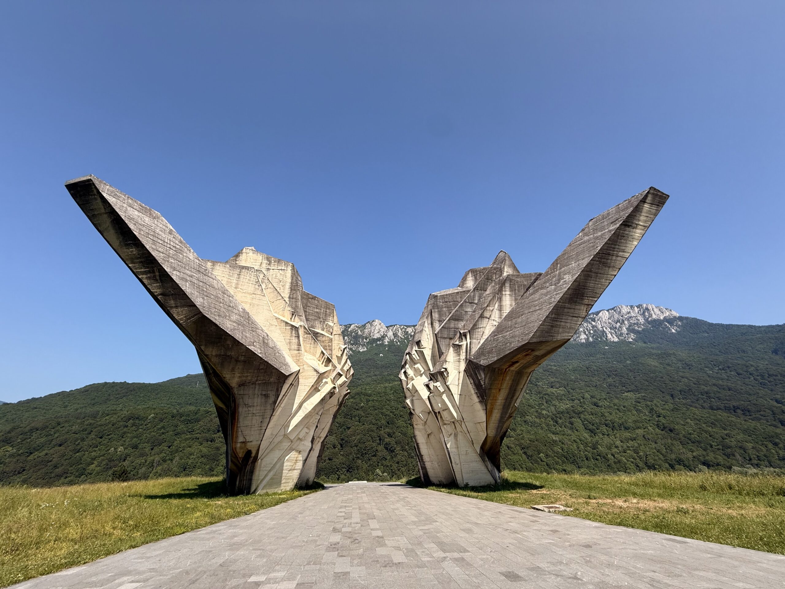 Denkmal im Tal der Helden: zwei hohe Betonflügel vor Bergkulisse